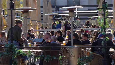 La-Gente-Se-Sienta-Al-Aire-Libre-En-Un-Restaurante-En-Estocolmo-Mientras-La-Gente-Pasa-En-Primer-Plano.