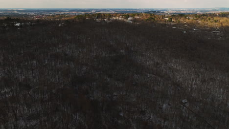 Mount-sequoyah's-dense-winter-forest-with-a-distant-cityscape-at-dusk,-aerial-view