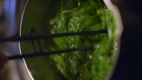 Green-vegetables-in-pot-of-boiling-water-stirred-with-tongs,-filmed-as-vertical-closeup-slow-motion-handheld-style-shot