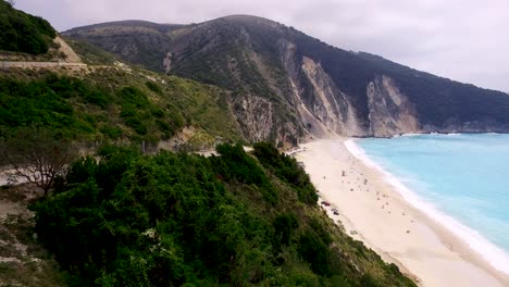 Coastal-view-of-Myrtos-Beach-in-Kefalonia,-Greece-with-turquoise-waters-and-mountain-backdrop,-aerial-view