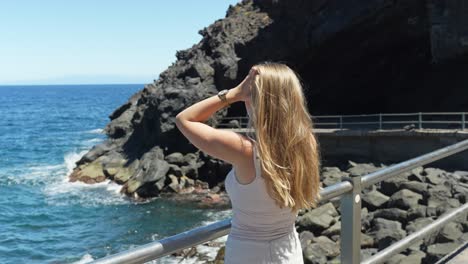 Hermosa-Rubia-Ajustando-El-Cabello-Mientras-Admira-La-Costa-De-La-Isla-De-Tenerife