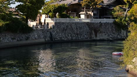 Cinematic-slow-tilt-up-reveal-of-ancient-Japanese-shrine-next-to-river