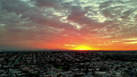 Sonnenuntergang-Wirft-Lebendige-Farben-über-Eine-Weitläufige-Stadtlandschaft,-Wolken-Malen-Einen-Dramatischen-Himmel,-Luftaufnahme