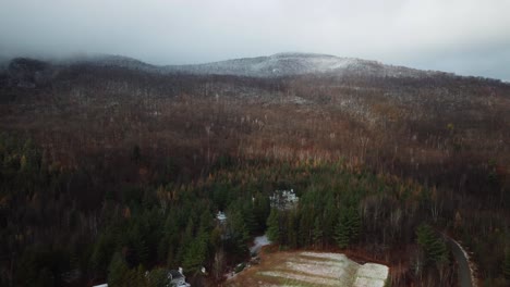 Aerial-shot-of-forest-and-mountain-with-a-little-bit-of-snow-and-clouds-on-top