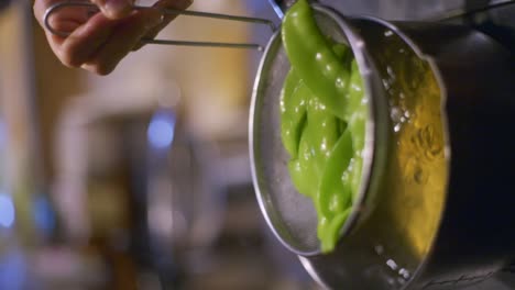 Snow-peas-in-strainer-being-drained-of-all-water-over-boiling-pot-of-broth,-filmed-as-vertical-closeup-slow-motion-shot