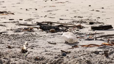 Close-up-of-a-plastic-bottle-amidst-debris-on-a-sandy-beach,-highlighting-pollution