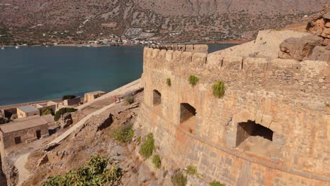 Drone-flies-alongside-historic-ruins-of-Spinalonga-as-travelers-explore-the-old-fortress
