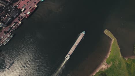 Un-Solo-Barco-Navegando-A-Lo-Largo-De-Un-Río-Sinuoso-Al-Lado-De-La-Arquitectura-Urbana,-Luz-Del-Día,-Vista-Aérea
