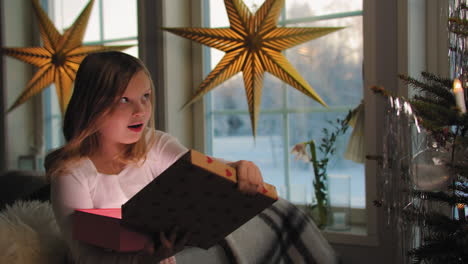 Una-Joven-Dulce-Reaccionando-Sorprendida-Abriendo-El-Regalo-En-La-Mañana-De-Navidad