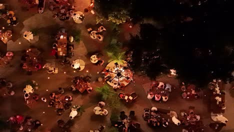 Vogelperspektive-über-Menschen,-Die-Sich-Nachts-Draußen-Um-Gut-Beleuchtete-Tische-Im-Dorf-Kura-Hulanda-In-Otrobanda,-Willemstad,-Curaçao-Versammelten