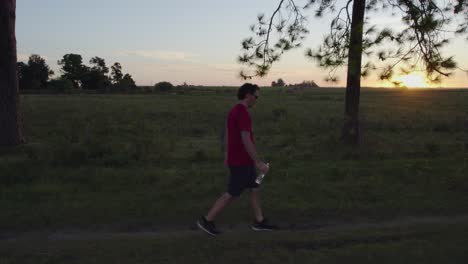 Young-man-walking-workout-stops-to-drink-water-in-nature-at-sunset