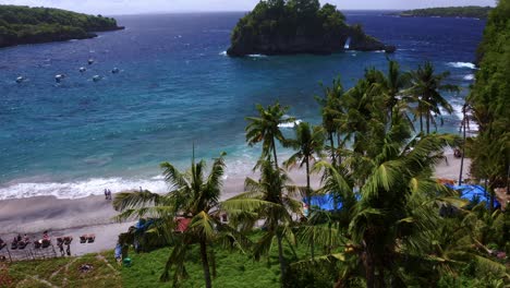 Beautiful-Turquoise-water-Shoreline-visible-through-the-top-of-Palm-trees---Crystal-Bay-beach,-Nusa-Penida---near-BALI,-Indonesia