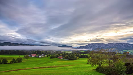 Time-Lapse,-Clouds-Moving-Fast-Above-Green-Wet-Agricultural-Meadow-Mountain-Sun-Shining-Above-trees-and-Rays-of-Light-through-misty-skyline