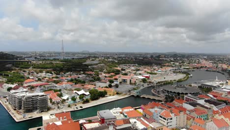 Panoramic-aerial-establishing-shot-of-Willemstad-iconic-orange-roofs-under-cloudy-skies