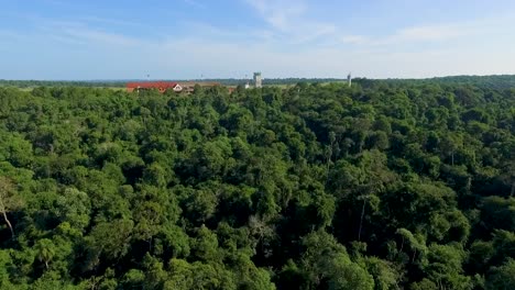 Lush-greenery-with-distant-farmhouses,-under-clear-skies,-aerial-view