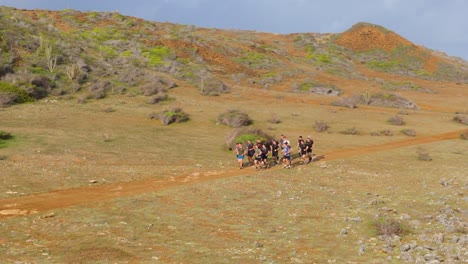 Group-of-men-run-together-in-pack-across-dry-arid-dirt-road-with-krumholz-wind-bent-shrubs