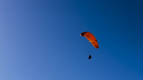 Paraglider-with-beautiful-orange-glider-flies-across-bright-blue-sky-at-Torrey-Pines-Gliderport-in-La-Jolla,-California