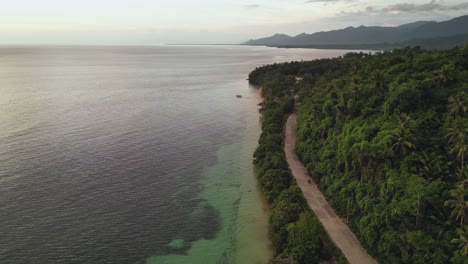 Toma-Aérea-Panorámica-De-Una-Isla-Tropical-Exuberante-Y-Aguas-Cristalinas-Del-Océano-Con-Motocicleta-Conduciendo-Por-La-Carretera-Costera