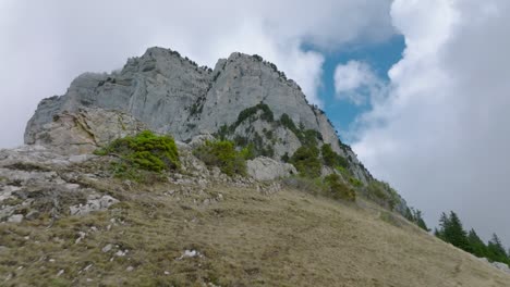 Climbing-hill-overtaking-cliff-to-impressive-rock-mountain,-French-Alps