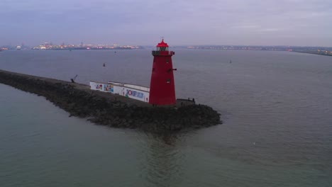 Drone-orbit-around-red-Poolbeg-lighthouse-with-view-of-Dublin-city-lights-in-distance