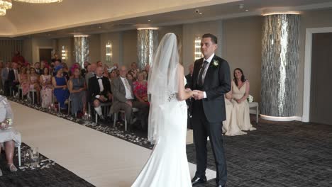 Bride-and-groom-exchange-vows-during-wedding-ceremony,-guests-look-on