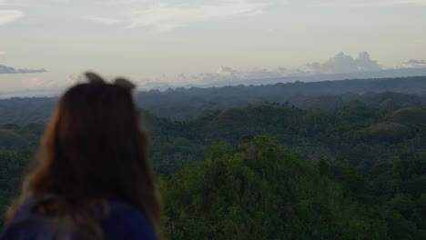 Woman-gazing-at-tropical-forest-landscape-during-sunrise,-back-to-camera,-tranquil-scene