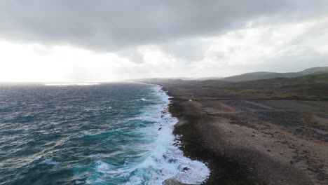 Drone-orbit-around-ocean-waves-crashing-along-wide-sprawling-coastline-off-to-horizon