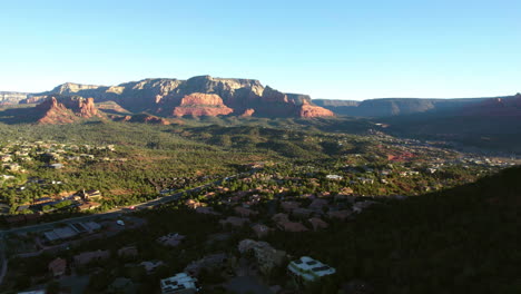 Drone-Shot-of-Sedona,-Arizona-USA,-Town-Buildings-in-Green-Valley-Under-Red-Rock-Hills-at-Sunrise