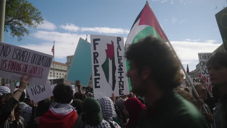Ein-Schild-Mit-Der-Aufschrift-„Free-Palestine“,-Das-Bei-Einer-Pro-Palästina-Demonstration-Hochgehalten-Wird,-Umgeben-Von-Fahnen-Und-Schildern