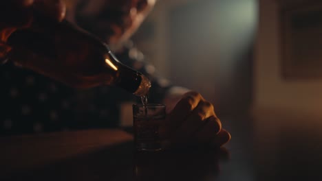 Slow-motion-shot-of-man-pouring-alcohol-in-a-glass-cup-from-a-bottle-with-blurred-background