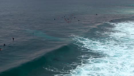 Drone-flying-backward-from-surfers-waiting-for-waves-in-Banzai-Pipeline-at-Ehukai-Beach-Park,-Ohau