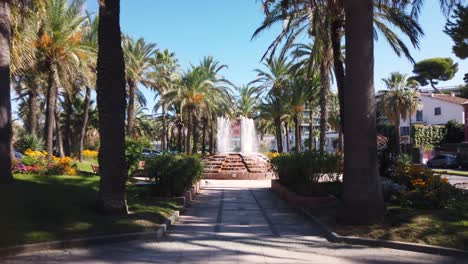Centered-shot-of-fountain-in-park,-cars-pass-on-road,-French-Riviera