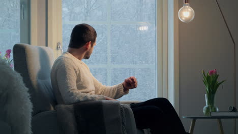 Man-in-sweater-looking-frustrated-and-angry-in-a-cozy-room-with-tulips-and-snow-outside,-side-view,-natural-light