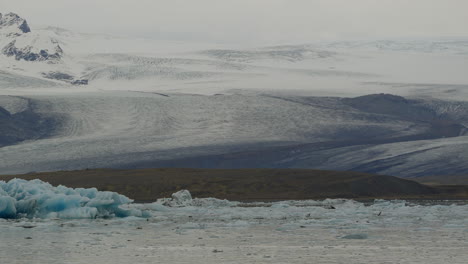 Laguna-Glaciar-En-Jökulsárlón,-Islandia,-Con-Glaciares-Flotando-En-Aguas-Heladas-Con-Montañas-Nevadas-Al-Fondo
