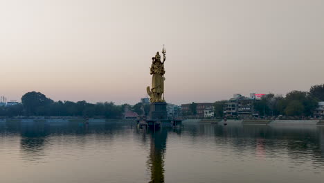 Disfrute-De-Una-Impresionante-Vista-Frontal-De-La-Inmensa-Estatua-Dorada-De-Lord-Shiva-En-El-Lago-Sursagar-En-Vadodara-Al-Atardecer
