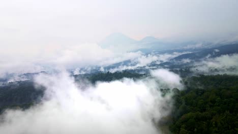 fast-movement-aerial-4k-drone-footage-of-Indonesia's-rich-rainforests-nestled-beside-a-national-park,-with-an-iconic-active-volcano-as-its-dramatic-backdrop