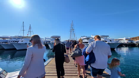 Los-Turistas-Caminan-A-Lo-Largo-De-Un-Embarcadero-En-Un-Puerto-De-Sharm-El-Sheikh-Hacia-Barcos-De-Lujo-Esperando-Para-Partir,-Egipto