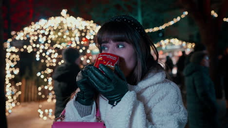 Beautiful-Woman-with-dark-Hair-saying-cheers-with-her-hand-and-drinking-Punch-from-red-Heart-Cup-at-Vienna-Christmas-Market-,-surrounded-by-Christmas-Lights-in-the-background