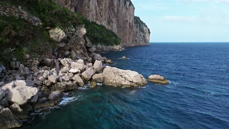 Cliffside-view-of-Capri's-rugged-coastline,-blue-sea,-sunny-day,-aerial-shot