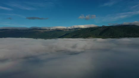 Vuelo-Lateral-Con-Dron-Sobre-Un-Mar-De-Nubes-Visualizando-Un-Gran-Sistema-Montañoso-Con-Bosques-Que-A-Su-Vez-Tiene-Una-Cadena-De-Nubes-En-Sus-Picos-Al-Amanecer-En-Un-Valle-Con-Un-Cielo-Azul-En-Avila-España