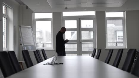 An-individual-strides-through-an-office-conference-room,-passing-by-a-lengthy-table-encircled-by-chairs,-symbolizing-the-essence-of-a-corporate-gathering-or-similar-professional-rendezvous