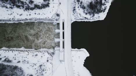 Toma-De-Establecimiento-Lento-Vista-Aérea-De-Drones-Agua-Corriendo-Notigi-Hidropresa-Río-Lago-Paisaje-Nevado-Invierno-Del-Norte-Manitoba-Canadá