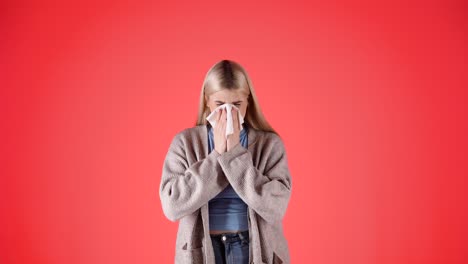 Helpless-young-woman-with-fever,-sneezing-in-napkin,-isolated-red-background
