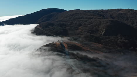 Colinas-Brumosas-Cubiertas-Por-Un-Manto-De-Nubes-Con-Un-Cielo-Azul-Claro-Arriba,-Toma-Aérea