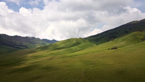 aerial-4k-drone-footage-of-the-tranquil-allure-of-a-lush-green-valley-nestled-among-mist-covered-hills,-enhanced-by-the-soothing-patter-of-cloudy-sky