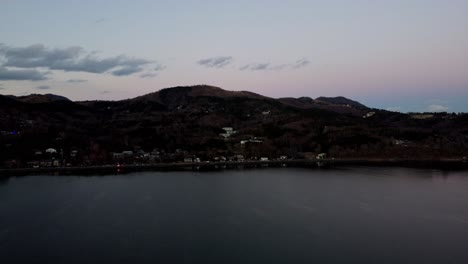 Twilight-hues-over-a-calm-lake-with-forested-hills,-serene-dusk-setting,-aerial-shot