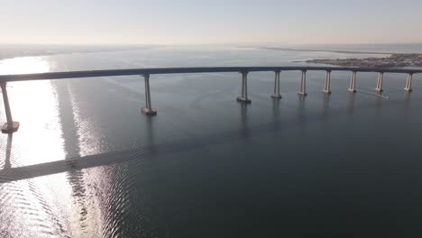 Coronado-Bridge-over-San-Diego-Bay,-as-sunshine-reflects-off-the-water,-aerial-wide-shot