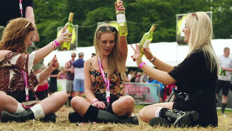 Three-young-girls-sitting-on-the-ground-enjoying-bottles-of-wine,-slow-motion