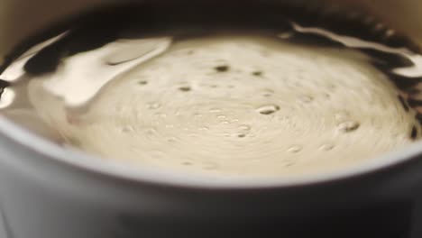 Slow-motion-top-view-of-a-cup-filled-with-coffee,-creating-a-swirl-after-stirring-with-a-spoon