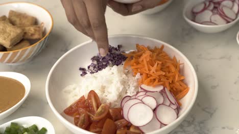 Adding-red-cabbage-to-a-vibrant-delicious-asian-fusion-poke-bowl-dish-bowl-with-rice-and-carrots